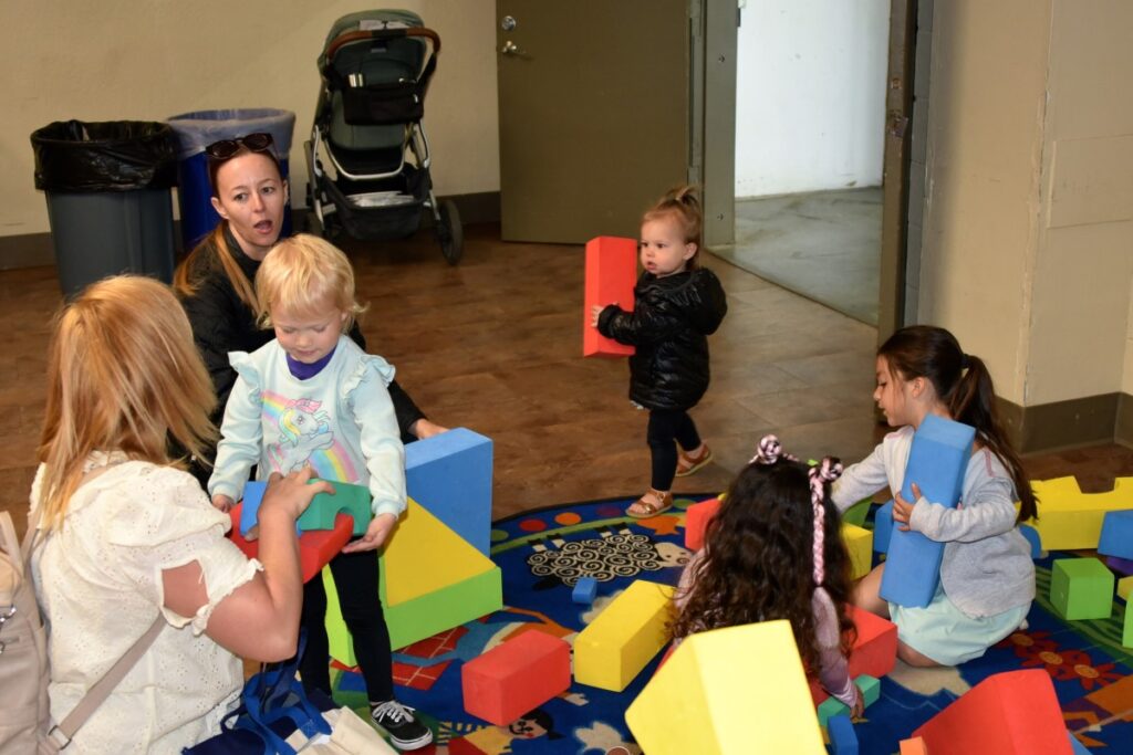 Two mothers supervise as children play with large foam blocks in a room set aside for them